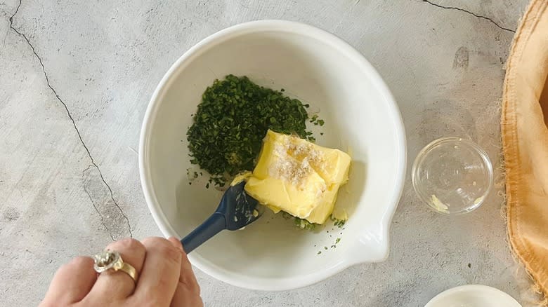 hand mixing butter with seasonings in white bowl