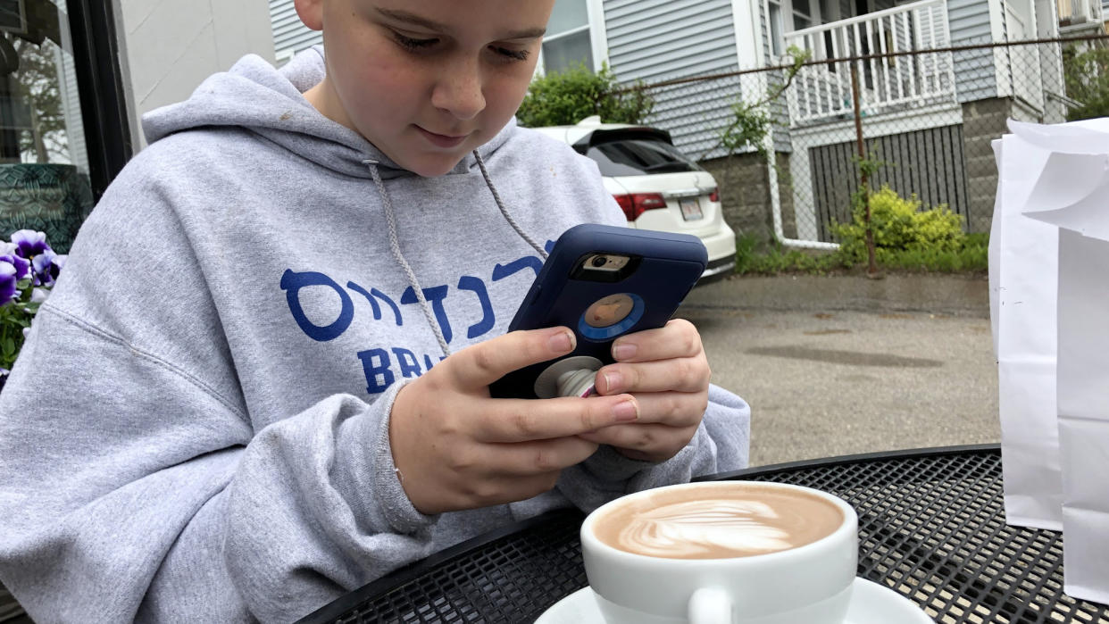  Child using an iPhone 11 in a large case with a fancy cappuccino in front 