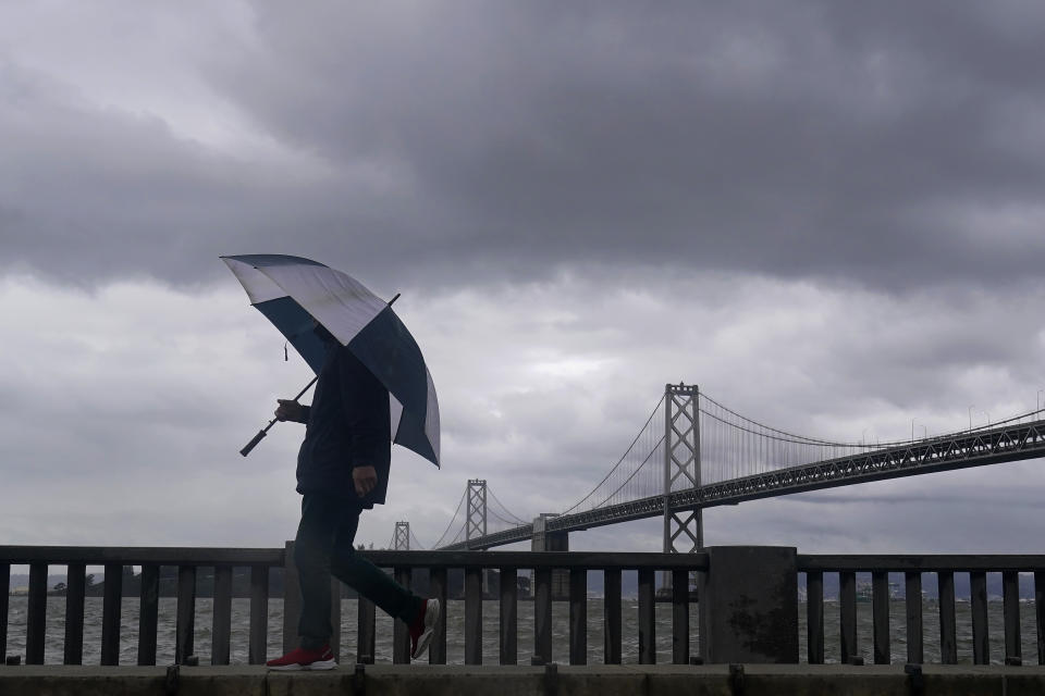 A pedestrian carries an umbrella while walking in front of the San Francisco-Oakland Bay Bridge in San Francisco, Tuesday, March 21, 2023. (AP Photo/Jeff Chiu)