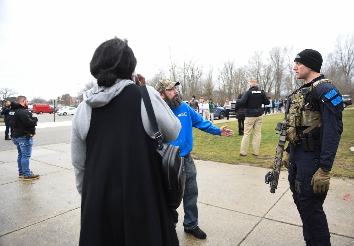 A trooper with the MSP Emergency Support (ES) team talks to a parent outside Okemos High School near the football field Tuesday, Feb. 7, 2023, after false 911 calls of a shooting. No students or staff were injured.
