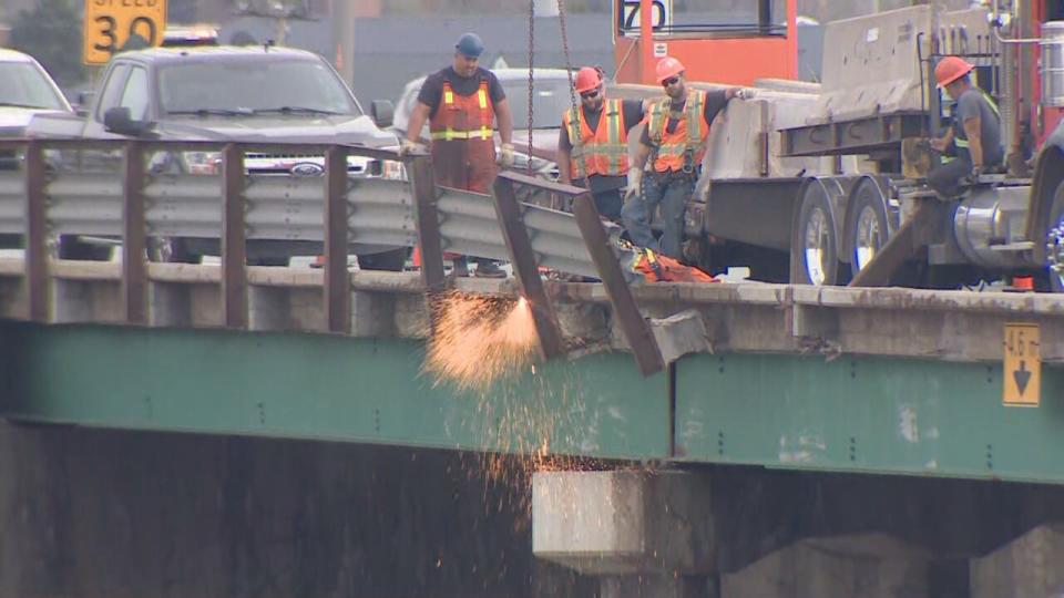 Construction workers remove guardrail from the overpass on Highway 101 after a tractor-trailer crashed through it.
