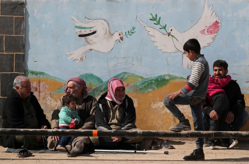 Internally displaced Syrians sit together near a mural in Azaz