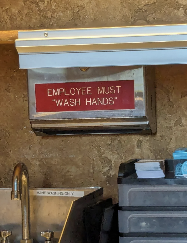 A metallic sign above a sink reads "EMPLOYEE MUST 'WASH HANDS.' " A smaller sign near the sink reads "HAND WASHING ONLY."