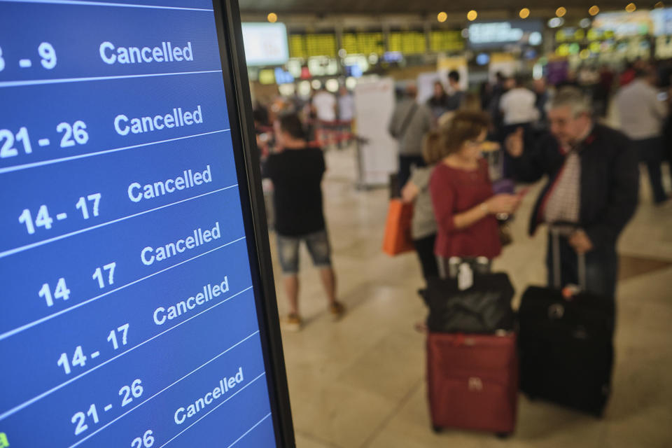 Passengers stand near a screen displaying cancelled flights in the airport in Santa Cruz de Tenerife, Spain, Sunday, Feb. 23, 2020. Flights leaving Tenerife have been affected after storms of red sand from Africa's Saharan desert hit the Canary Islands. (AP Photo/Andres Gutierrez)