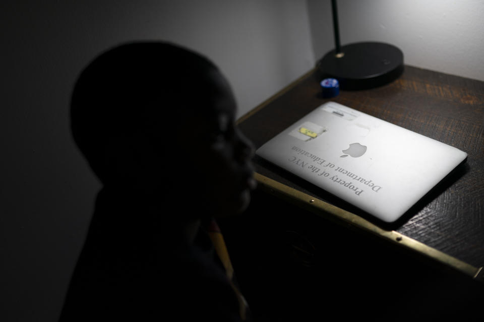 Adam Schneider, 7, center, sits with his older brother Isaiah in their bedroom while a city-issued laptop lies closed on the table, Wednesday, Dec. 8, 2021, in the Brooklyn borough of New York. The two boys received their computers midway through the COVID-19 pandemic and have needed them exchanged or replaced twice, a process that can take weeks to complete. (AP Photo/John Minchillo)