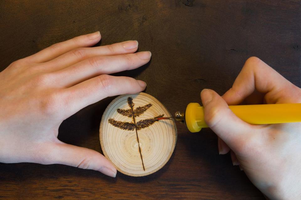 female hands burn out a tree twig sign with soldering iron on wooden disc