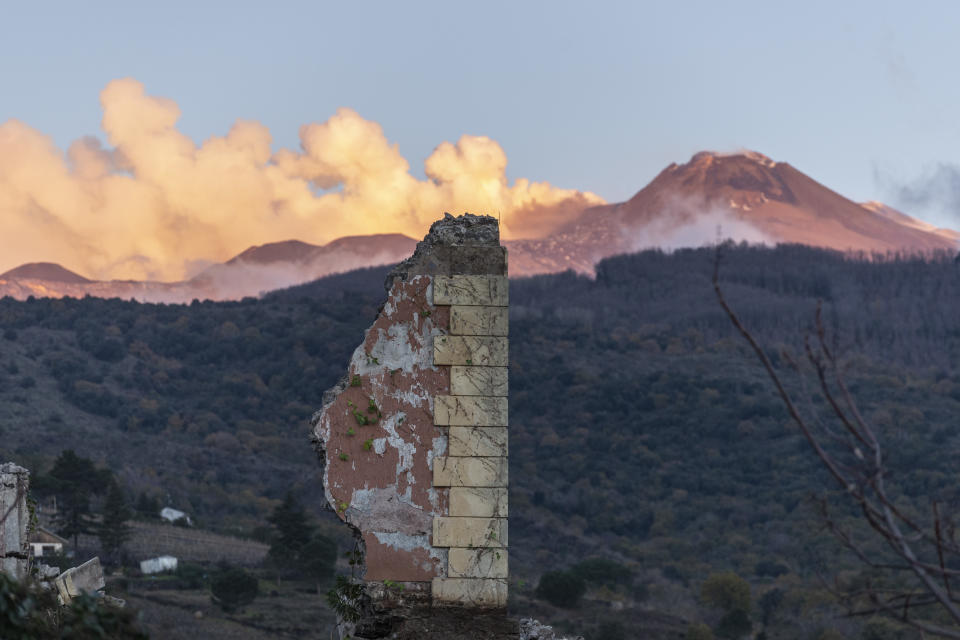 The remains of a collapsed structure are backdropped by plumes of smoke coming out Mount Etna volcano in Fleri, Sicily Italy, Wednesday, Dec. 26, 2018. A quake triggered by Italy's Mount Etna volcano has jolted eastern Sicily, slightly injuring 10 people and prompting frightened Italian villagers to flee their homes. (AP Photo/Salvatore Allegra)