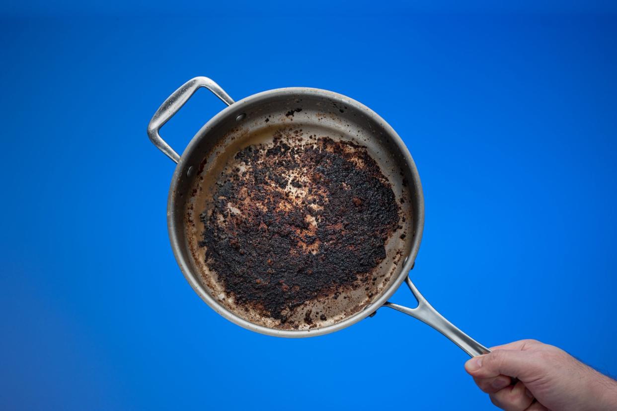 Dirty oily burnt metal frying pan held in hand by male hand.