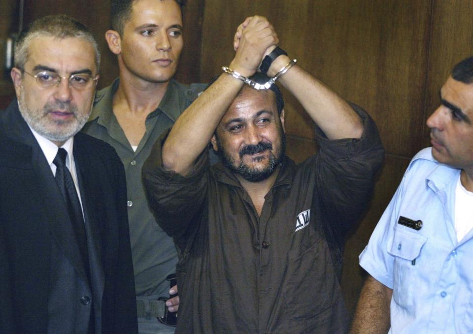 FILE - Marwan Barghouti, center, raises his handcuffed hands in the air on the opening day of his trial at Tel Aviv's District Court on Aug. 14, 2002. Hamas officials say that any cease-fire deal with Israel should include the release of prisoner Marwan Barghouti — a leader of the militant group's main political rival. The demand by Hamas marks the central role Barghouti plays in Palestinian politics — even after more than two decades behind bars and sentenced by Israel to multiple life terms in prison. (AP Photo/Brennan Linsley, File)