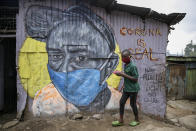 FILE - In this April 18, 2020, file photo, a boy wearing a face mask carries a small bowl of "githeri", or mixed beans and maize, for him to eat as he walks past a mural warning people about the risks of the coronavirus, painted by graffiti artists from the Mathare Roots youth group, in the Mathare slum, of Nairobi, Kenya. A dangerous stigma has sprung up around the coronavirus in Africa — fueled, in part, by severe quarantine rules in some countries as well as insufficient information about the virus. (AP Photo/Brian Inganga, File)