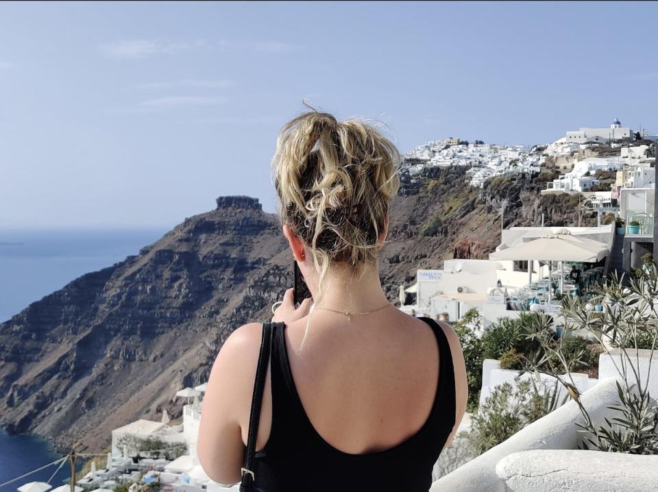 the writer with her back to the camera overlooking a cliff in santorini at white houses and blue water