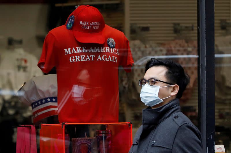 FILE PHOTO: A man in a surgical mask walks by goods for sale emblazoned with U.S. President Donald Trump's 2016 campaign slogan "Make America Great Again", after more cases of coronavirus were confirmed in New York City