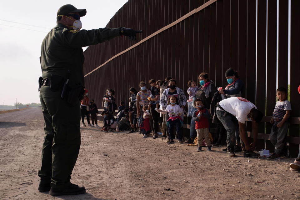 A U.S. Border Patrol agent instructs asylum-seeking migrants as they line up along the border wall after crossing the Rio Grande river into the United States from Mexico on a raft, in Penitas, Texas, on March 17, 2021. / Credit: ADREES LATIF / REUTERS