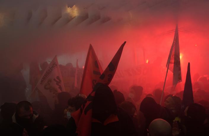 A large crowd of protesters waving flags and lighting flares inside of LVMH's headquarters.