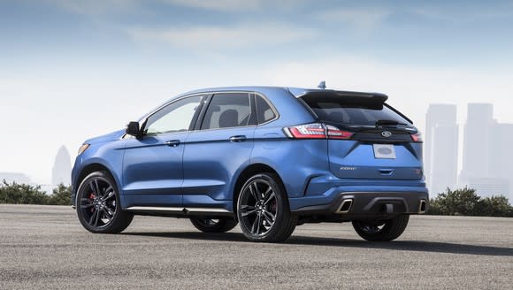 A blue Edge ST, a version of the midsize Edge SUV with sporty black wheels and a rear spoiler, parked with a city skyline visible in the background.