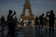 FILE - People use their smartphones near the Olympic rings that are displayed on the Eiffel Tower in Paris, June 7, 2024 in Paris. Cybersecurity experts and French officials say Russian disinformation campaigns against France are zeroing in on legislative elections and the Olympic Games which open in Paris at the end of the month. (AP Photo/Aurelien Morissard, File)