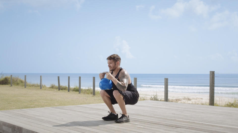 Luke Zocchi performs a goblet squat with a kettlebell