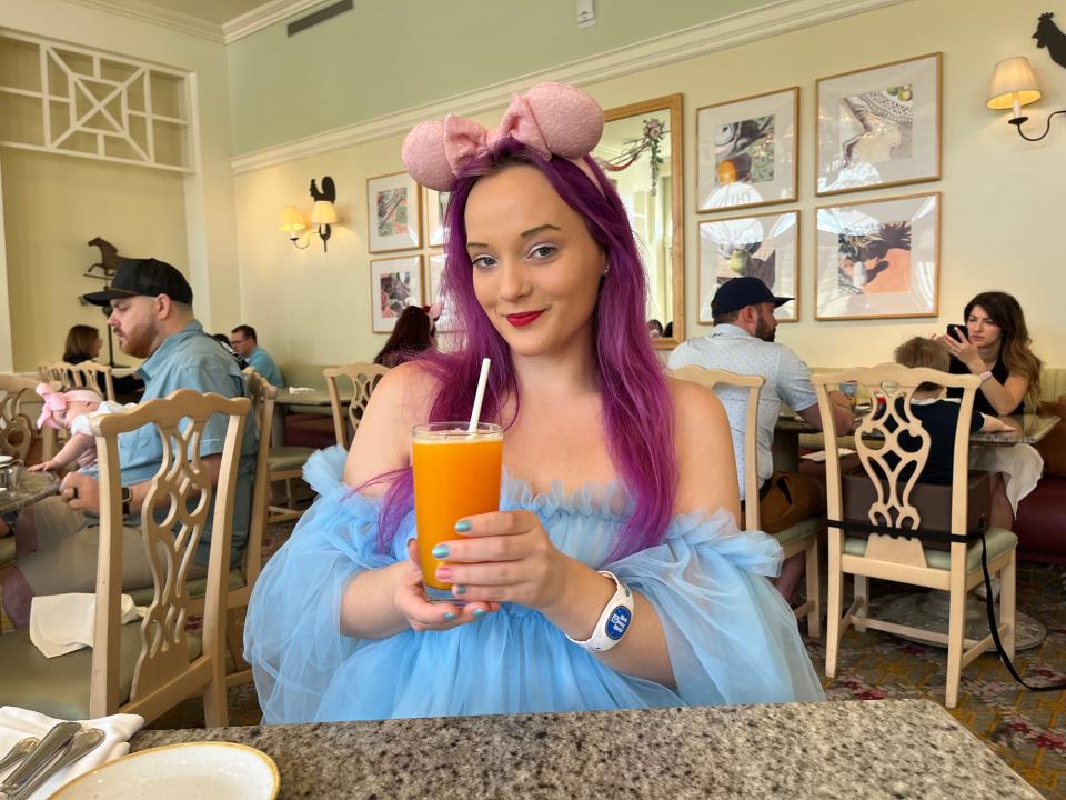 jenna posing with a glass of pog juice at a table in the grand floridian cafe