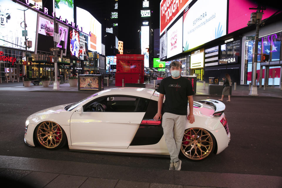 In this Saturday, May 2, 2020 photo, Danny Lin poses for photos with his 2008 Audi R8 in New York's Times Square during the coronavirus pandemic. "I never bring my car here," said the 24-year-old from Queens. "Only for today, to get some cool shots." (AP Photo/Mark Lennihan)