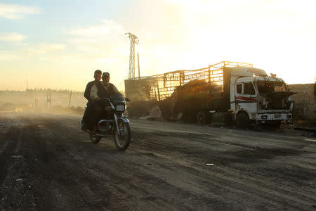 Men drive a motorcycle near a damaged aid truck after an airstrike on the rebel held Urm al-Kubra town, western Aleppo city, Syria September 20, 2016. REUTERS/Ammar Abdullah