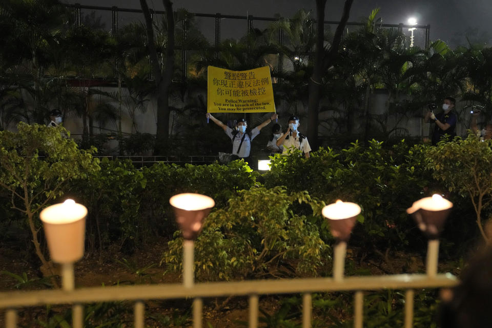 A police officer holds up a placard to warn people lighting candles to mark the anniversary of the military crackdown on a pro-democracy student movement in Beijing, outside Victoria Park in Hong Kong, Friday, June 4, 2021. A member of the committee that organizes Hong Kong's annual candlelight vigil for the victims of the Tiananmen Square crackdown was arrested early Friday on the 32nd anniversary. (AP Photo/Kin Cheung)