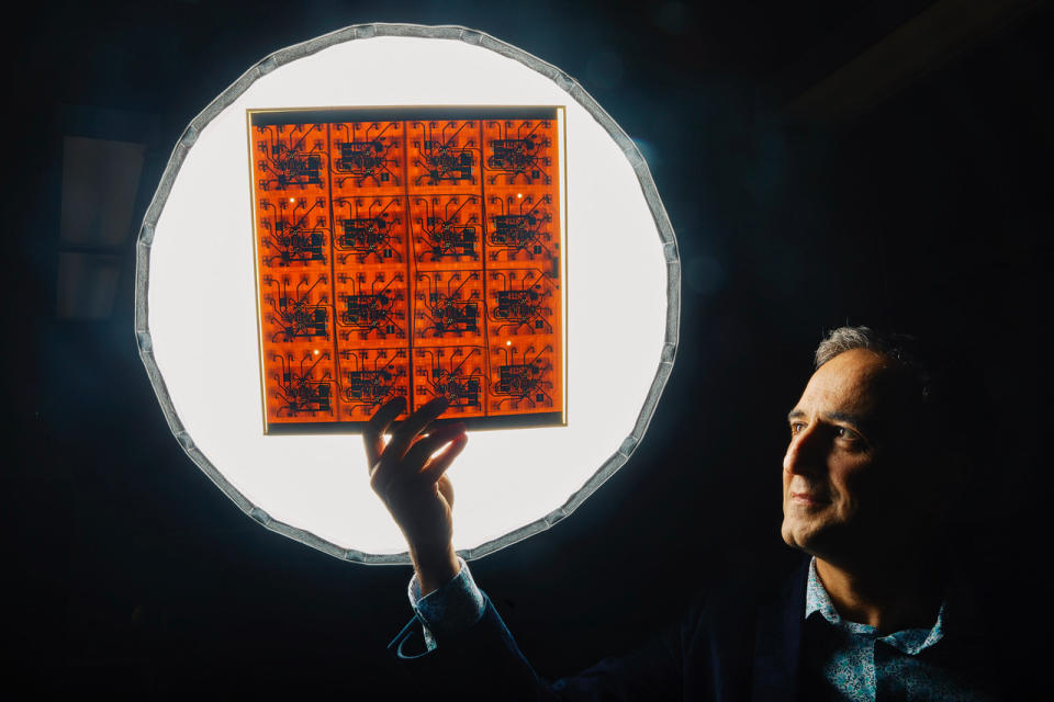 a man against a dimly lit wall holds up a transparent sheet with an orange colored grid in front of a brightly lit circle.