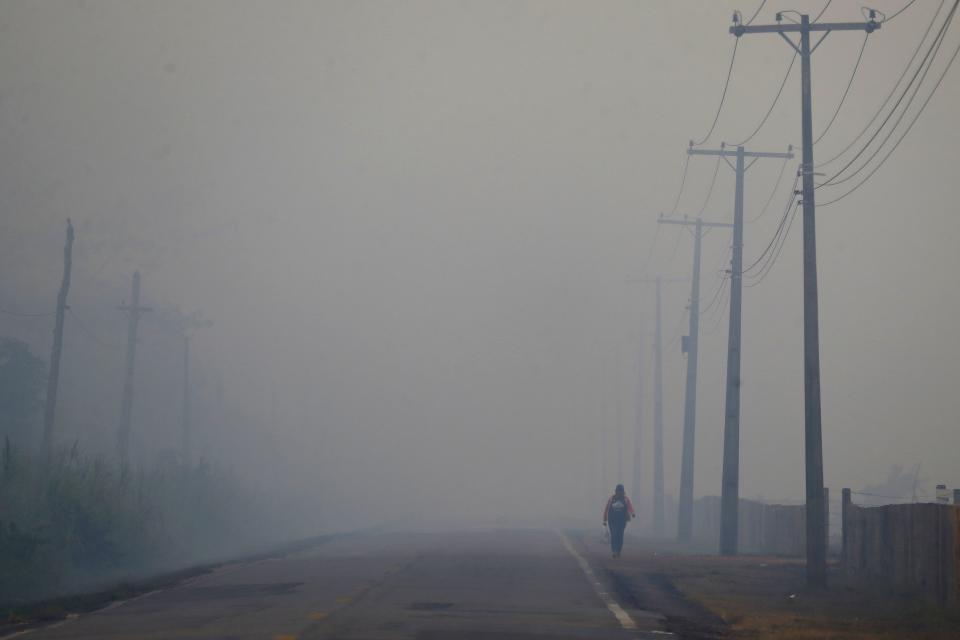 FILE - A person walks on the BR-319 highway through smoke from a forest fire that reaches Careiro Castanho in Brazil's Amazonas state, Sept. 6, 2023. (AP Photo/Edmar Barros, File)