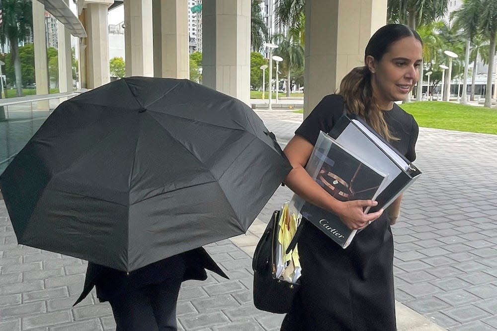 Celebrity handbag designer Nancy Gonzalez hides under a black umbrella as she walks with her lawyer Andrea Lopez outside the federal courthouse Monday, April 22, 2024, in Miami.