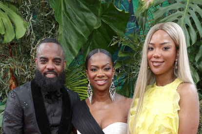 Kandi, Todd, and Riley pose together in front of foliage in formal attire.