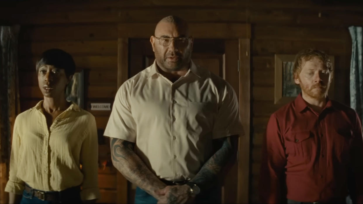  Abby Quinn, Nikki Amuka-Bird, Dave Bautista, and Rupert Grint stand in a line in the cabin in Knock at the Cabin. 