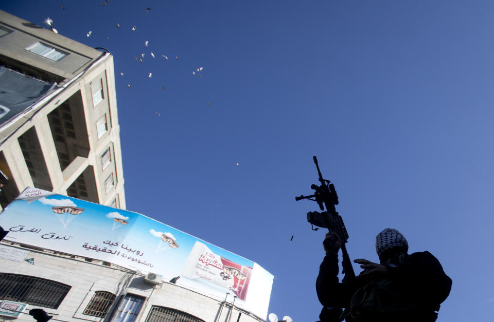 Birds scatter as a masked Palestinian shoots in the air during a celebration marking the 55th anniversary of the Fatah movement, in the West Bank city of Ramallah, Tuesday, Dec. 31, 2019. (AP Photo/Majdi Mohammed)