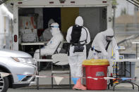 In this Tuesday, June 16, 2020, photo, Washington National Guard medics wear full protective equipment as they prepare to test a driver at a coronavirus test site in Yakima, Wash. Yakima, Benton and Franklin counties remain in Phase 1, meaning only essential businesses are open; restaurant service is limited to takeout and delivery; and limited outdoor recreation. (AP Photo/Elaine Thompson)