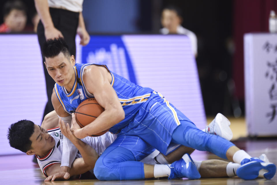 Jeremy Lin in a blue uniform holds a ball on the ground over an opponent. 