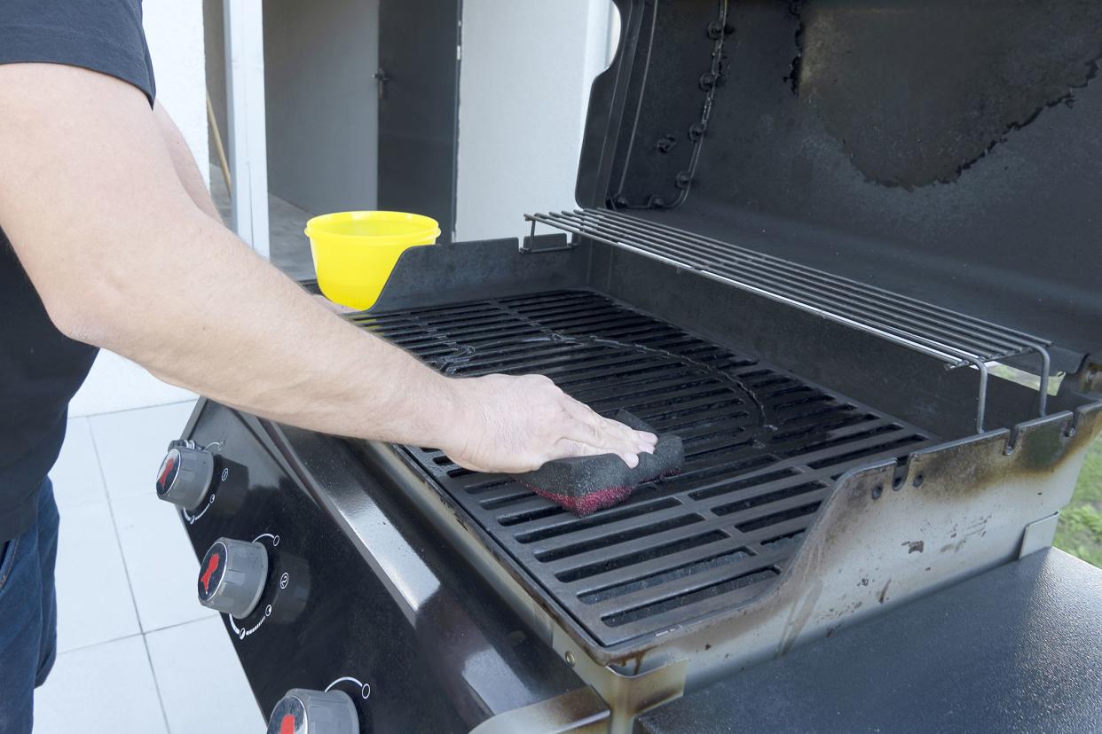 The male hand cleans the black grill with a soft brush. Grill for frying meat. Cleaning the outdoor gas grill in the backyard.