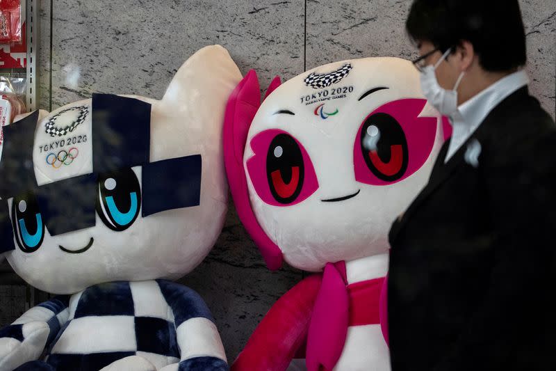 FILE PHOTO: A man wearing a protective face mask, following an outbreak of the coronavirus disease (COVID-19), walks past Tokyo 2020 Olympic Games mascot Miraitowa and Paralympic mascot Someity plushies at a building in Tokyo