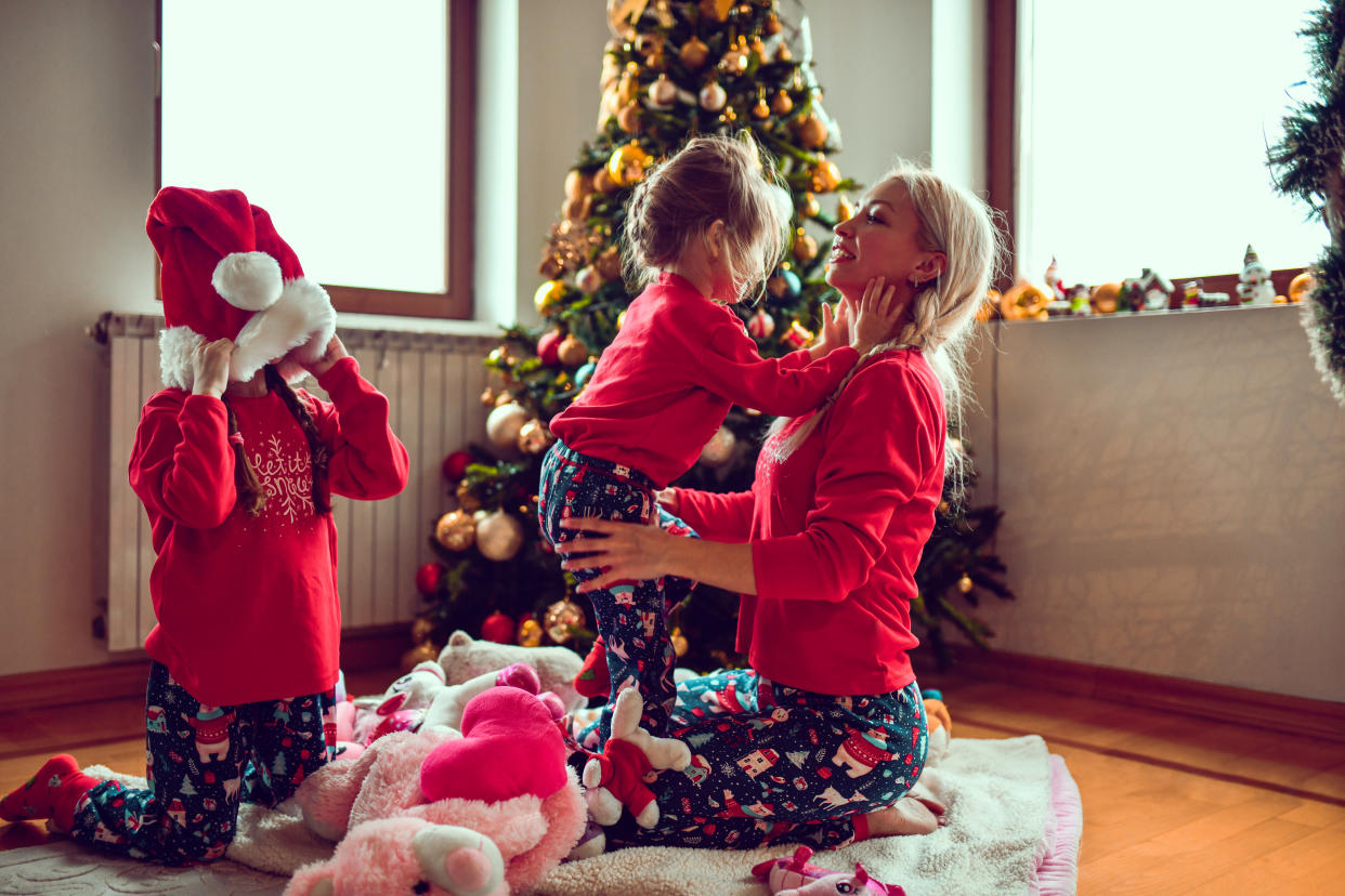 Mother And Daughters Wearing Matching Christmas Pajamas While Playing Under Christmas Tree