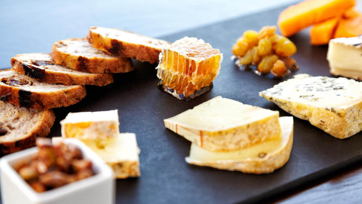 Fancy cheese plate with blue cheese, cheddar, goat cheese, bread, honey and pistachios at a luxury restaurant.