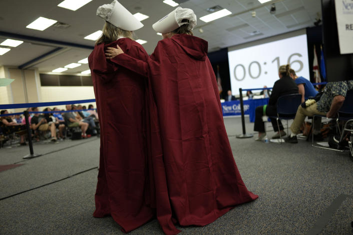 Two members of a group of parents of New College of Florida current students and a recent alum who came dressed as handmaids from Margaret Atwood's "The Handmaid's Tale," talk together as they wait to give public comment during a meeting of the college's board of trustees, Tuesday, Feb. 28, 2023, in Sarasota, Fla. The conservative-dominated board of trustees of Florida's public honors college was meeting Tuesday to take up measures making changes in the school's diversity, equity and inclusion programs and offices.(AP Photo/Rebecca Blackwell)