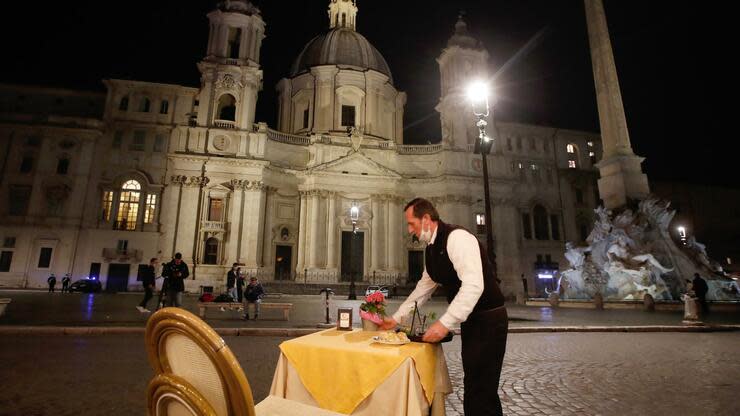 Ein Kellner räumt einen Tisch in einem Café-Restaurant auf der Piazza Navona in Rom vor Beginn der Ausgangssperre ab. Foto: dpa