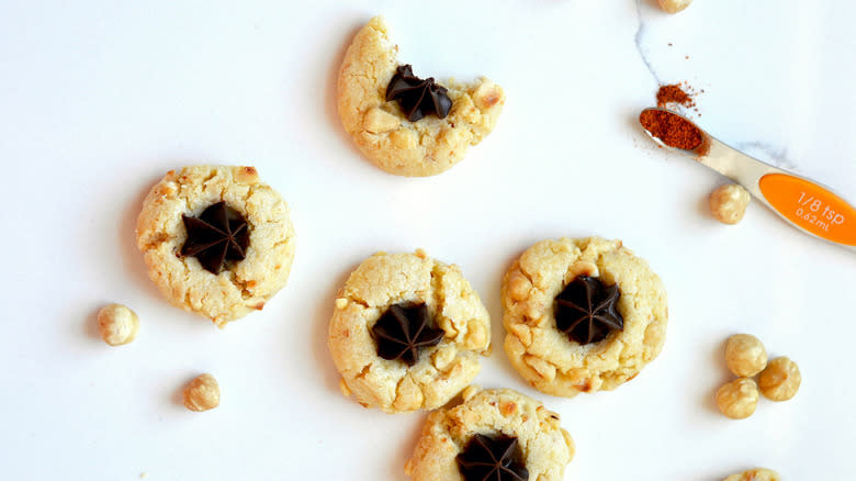 Chile chocolate hazelnut thumbprint cookies on a countertop, with scattered hazelnuts and cayenne powder