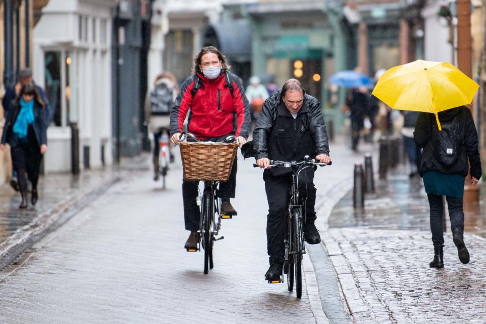 People cycle through rain through rain on Trinity Street in Cambridge (PA)