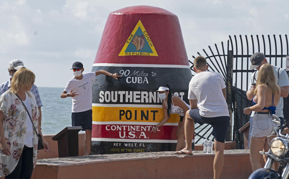 In this photo provided by the Florida Keys News Bureau, visitors gather at the Southernmost Point marker Friday, Jan. 7, 2022, in Key West, Fla. City of Key West Public Works employees completed restoration of the iconic marker late Thursday, after it was scorched early New Year's Day when two men burned a Christmas tree next to it. Both men were served warrants and charged with criminal mischief with damages over $1,000. The Southernmost Point marker is one of the most popular landmarks in the Florida Keys. (Rob O'Neal/Florida Keys News Bureau via AP)