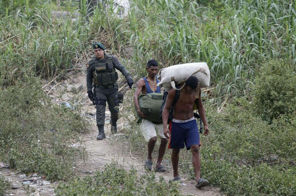 A Colombian police officer detains two smugglers who crossed the border illegally in La Parada, on the outskirts of Cucuta, Colombia, on the border with Venezuela, Tuesday, Feb. 5, 2019. Venezuelan opposition leader Juan Guaido is moving ahead with plans to try to bring in humanitarian aid through the Colombian border city of Cucuta, where the U.S. government will transport and store food and medical supplies destined for Venezuela. (AP Photo/Fernando Vergara)