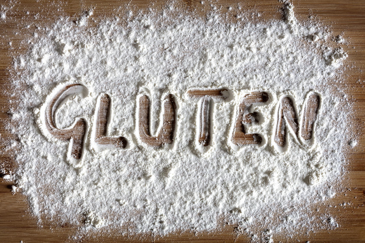 Palabra de gluten escrita en harina en el concepto de tablero para hornear para el cuidado de los alérgenos y la intolerancia