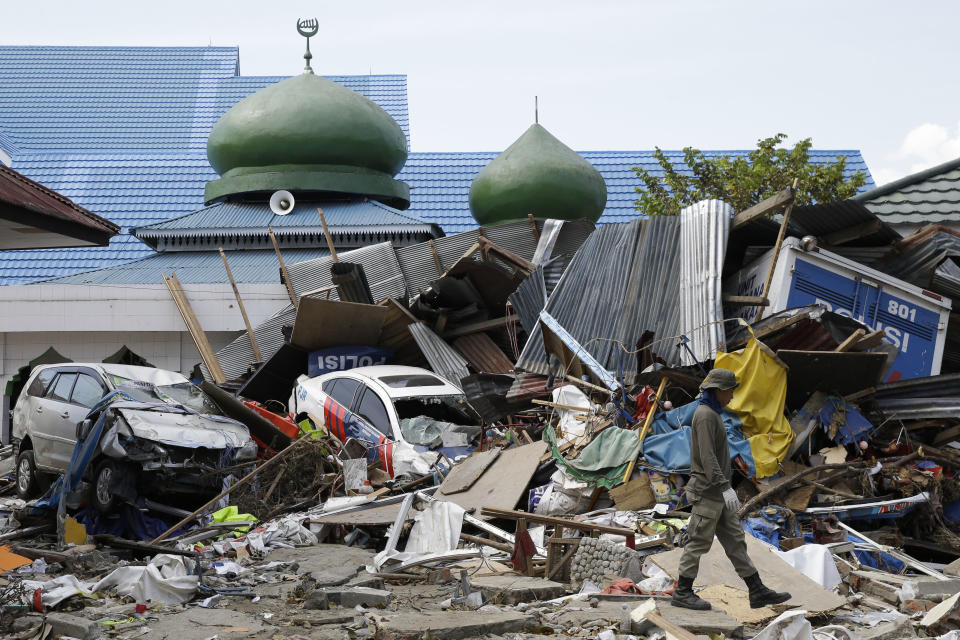 A man walks past ruins of cars and structures destroyed in the massive earthquake and tsunami that hit Palu, Central Sulawesi, Indonesia Thursday, Oct. 4, 2018. Life is on hold for thousands living in tents and shelters in the Indonesian city hit by a powerful earthquake and tsunami, unsure when they'll be able to rebuild and spending hours each day often futilely trying to secure necessities such as fuel for generators. (AP Photo/Aaron Favila)