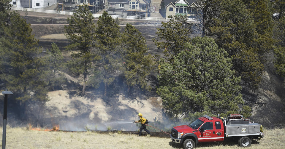 A firefighter knocks down flames trying to come up out of the ravine where a fire occurred on Friday, April 22, 2022, in Colorado Springs, Colo. The fire came to just across the road from houses, some still under construction in northern Colorado Springs. Homes were evacuated in the area, because of the gusting winds, some up to 50 mph. (Jerilee Bennett/The Gazette via AP)