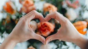 Woman forming a heart with hands against flower bouquet. Heart made with hands. Receiving flower bouquet delivery on Valentine’s day. Online dating concept. Long distance relationship. Dating anniversary.