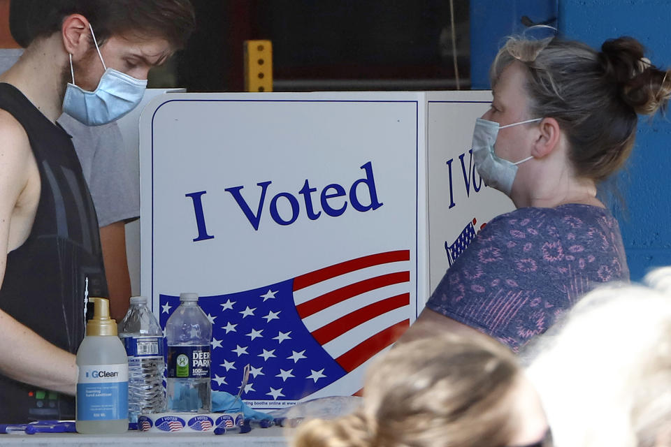 A voter fills out his ballot as a woman waits her turn during primary voting at the public safety building in McKeesport, Pa., Tuesday, June 2, 2020. (AP Photo/Gene J. Puskar)