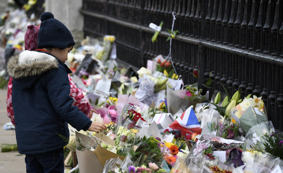 A child looks at flowers left outside the gates of Buckingham Palace in London, a day after the death of Britain's Prince Philip, Saturday, April 10, 2021. Britain's Prince Philip, the irascible and tough-minded husband of Queen Elizabeth II who spent more than seven decades supporting his wife in a role that mostly defined his life, died on Friday. (AP Photo/Alberto Pezzali)