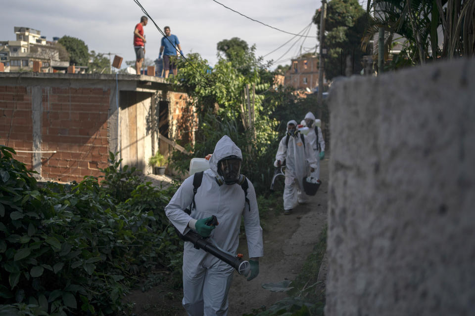 Volunteers spray disinfectant in an alleyway to help contain the spread of the new coronavirus in the Babilonia slum of Rio de Janeiro, Brazil, Sunday, July 12, 2020. (AP Photo/Leo Correa)